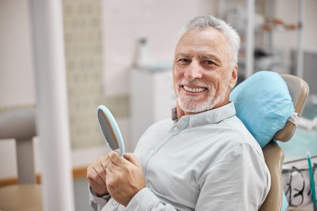 Man with loose tooth looking in handheld mirror